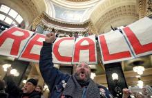 Image of protesters in a government holding a large banner that says "RECALL"